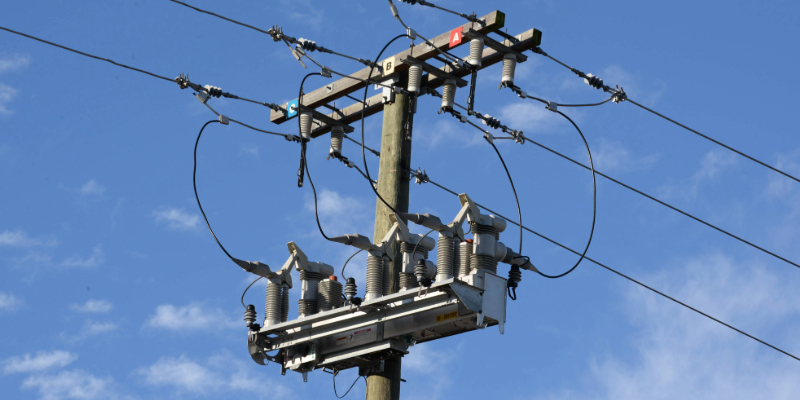 Medium-range framing of a pole-mounted IntelliRupter fault interrupter set against a blue sky with wispy white clouds.
